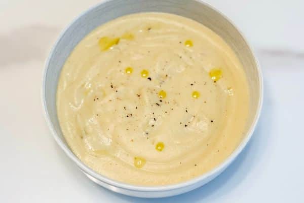 A bowl of silky smooth plant-based creamy cauliflower soup with a drizzle of truffle oil and freshly cracked black pepper.
