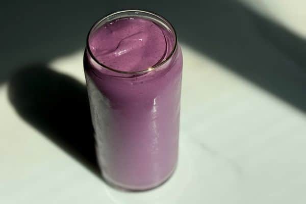 Overhead view of a creamy high protein plant-based peanut butter and jelly smoothie in a glass can cup on a dark marble surface with dramatic shadow lighting.