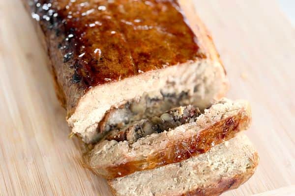 Sliced stuffed vegan roast with a glossy maple-soy glaze on a bamboo cutting board, showing the mushroom and pecan stuffing spiraled through the center.