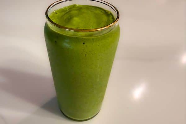 A vibrant green high protein plant-based super green smoothie in a gold rimmed glass cup on a white surface, thick and creamy in texture.