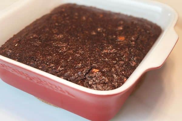 Freshly baked vegan brownies with melted chocolate chips, cooling in a red ceramic baking dish.