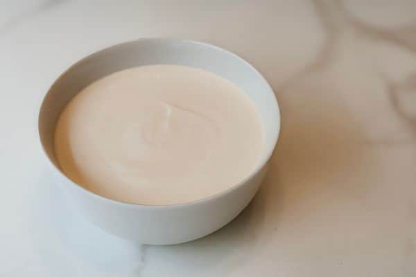 A smooth, creamy vegan yogurt made with a coconut milk and soy milk base, served in a white ceramic bowl on a marble surface.
