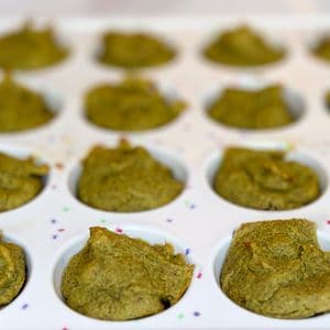 Close up of green plant-based baby-led weaning mini muffins freshly baked in a white confetti mini muffin tray, showing the soft texture and domed tops perfectly sized for baby fingers.