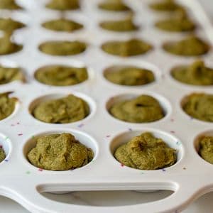 Straight on view of a full tray of green plant-based baby-led weaning mini muffins in a white confetti mini muffin tray on a marble surface, showing the full batch yield.