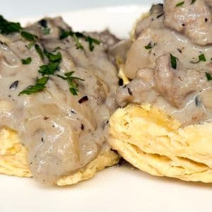 Close up of creamy plant-based beyond meat gravy smothering flaky vegan biscuits garnished with fresh chopped parsley showing the rich thick texture of the gravy.