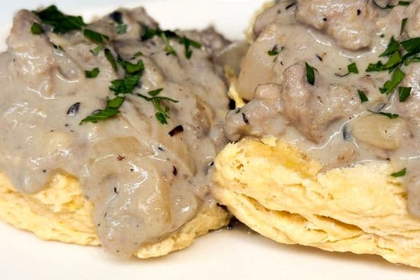 Close up of creamy plant-based beyond meat gravy smothering flaky vegan biscuits garnished with fresh chopped parsley showing the rich thick texture of the gravy.