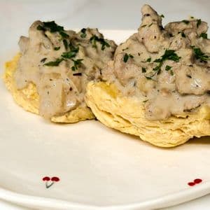 Two fluffy vegan biscuits topped with creamy plant-based beyond meat gravy garnished with fresh chopped parsley on a white cherry patterned plate.