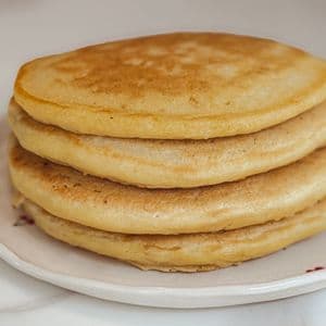 A stack of four golden fluffy vegan buttermilk pancakes on a white cherry patterned plate on a marble surface.