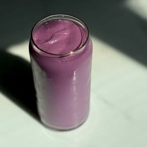 Overhead view of a creamy high protein plant-based peanut butter and jelly smoothie in a glass can cup on a dark marble surface with dramatic shadow lighting.