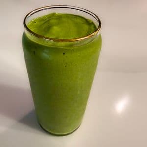 A vibrant green high protein plant-based super green smoothie in a gold rimmed glass cup on a white surface, thick and creamy in texture.