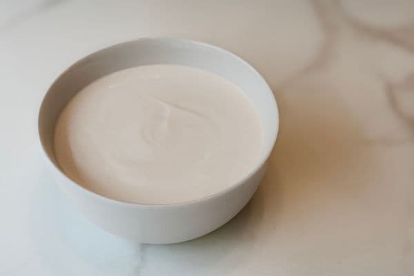 A smooth, creamy vegan yogurt made with a coconut milk and soy milk base, served in a white ceramic bowl on a marble surface.