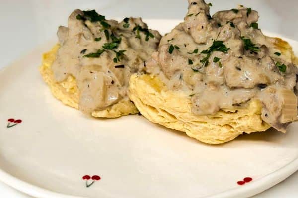 Two fluffy vegan biscuits topped with creamy plant-based beyond meat gravy garnished with fresh chopped parsley on a white cherry patterned plate.