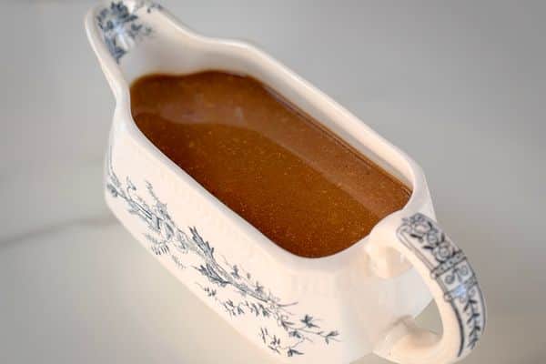 Smooth vegan brown gravy in a vintage white gravy boat with blue floral transferware pattern on a white marble surface.