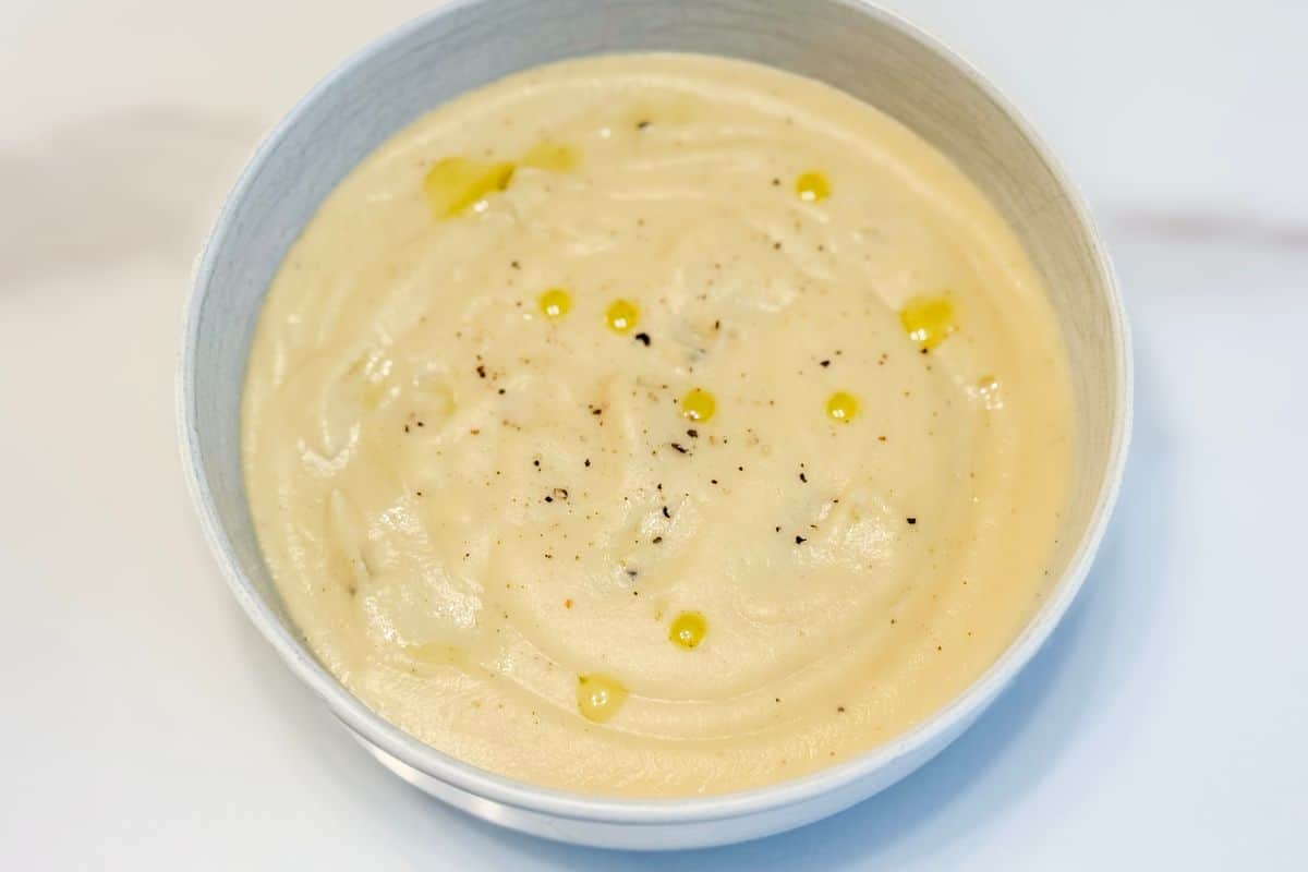 A bowl of silky smooth plant-based creamy cauliflower soup with a drizzle of truffle oil and freshly cracked black pepper.