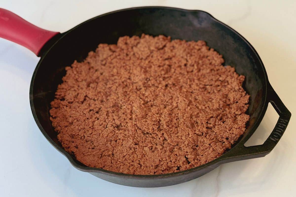 Homemade vegan ground beef made with TVP displayed in a cast iron skillet with a red silicone handle, photographed on a marble surface.