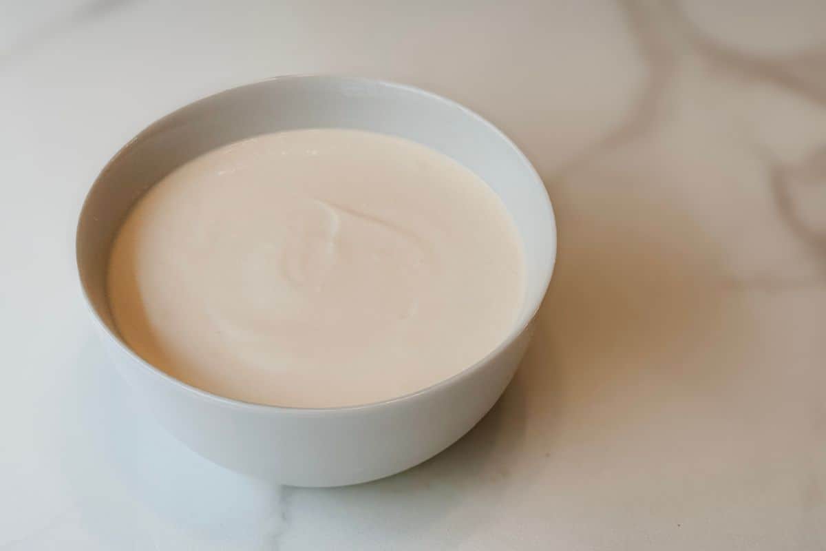 A smooth, creamy vegan yogurt made with a coconut milk and soy milk base, served in a white ceramic bowl on a marble surface.